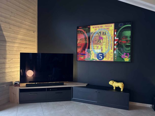 Coin TV moderne avec meuble en bois et noir mat, mur contrasté avec une œuvre d'art colorée, éclairage d'ambiance et décoration minimaliste incluant une sculpture jaune et des finitions en bois naturel.